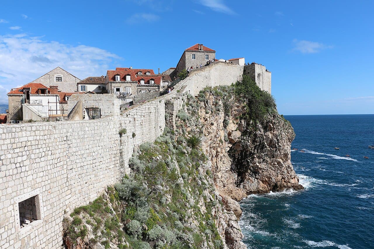 The city walls of Dubrovnik running above the sea under a clear sky