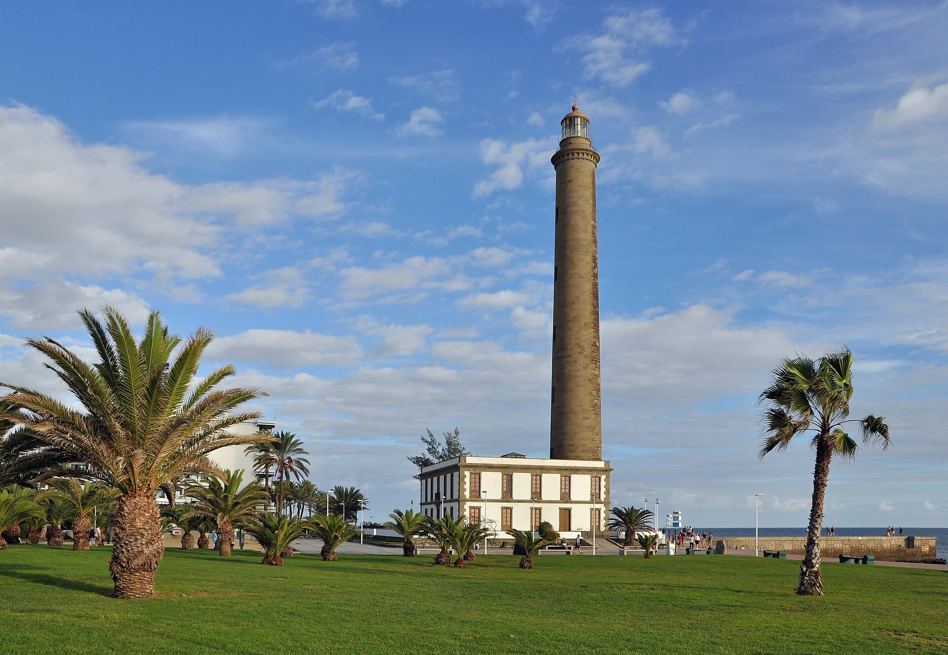 The Maspalomas lighthouse rising above palm trees and a lawn under a blue sky