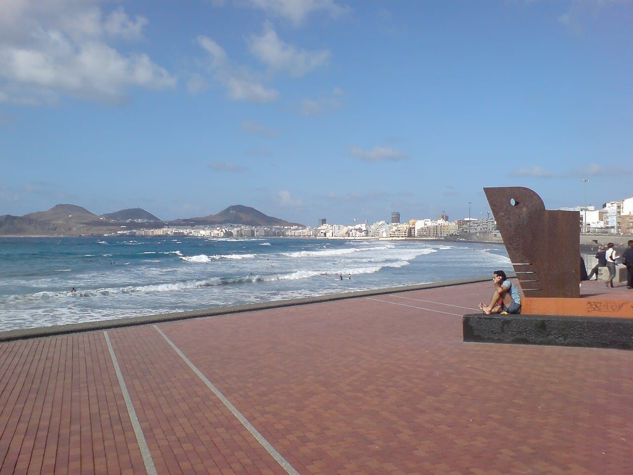 The Paseo de Las Canteras promenade beside the beach, with a sculpture in the foreground