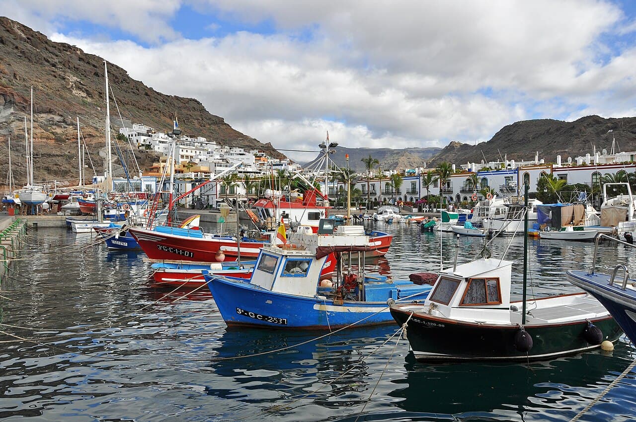 Colourful fishing boats in the harbour of Puerto de Mogán, below the valley slopes