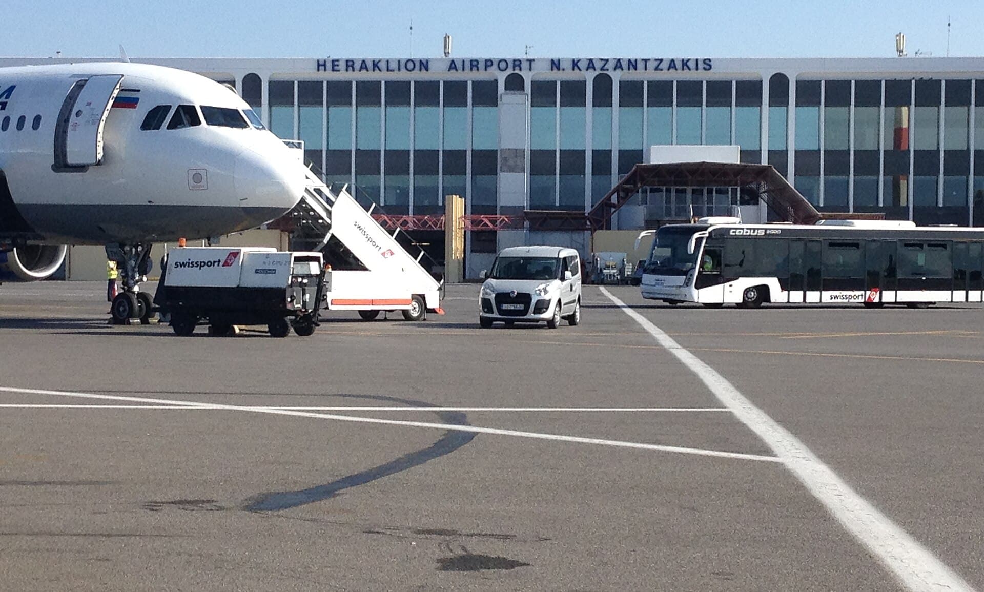 The terminal building at Heraklion Airport seen from the apron, with an aircraft and an airport bus