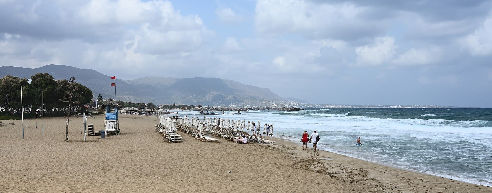 The beach at Malia with sunbeds along the shore and mountains in the distance
