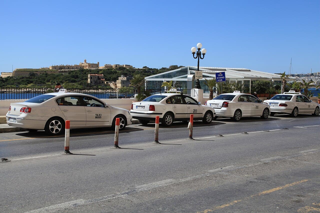 White Maltese taxis waiting in a rank by the sea