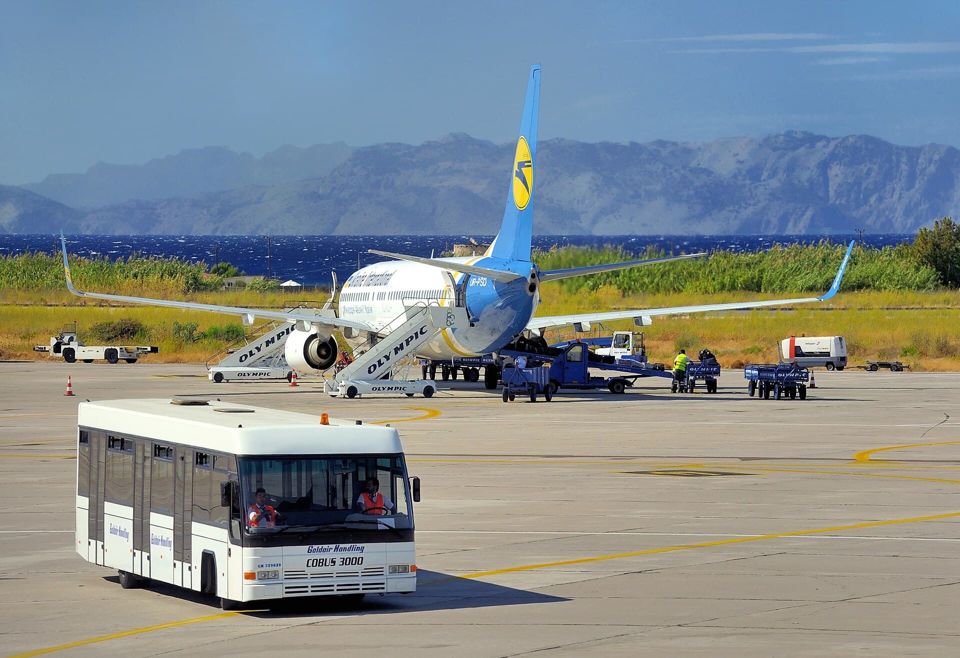 Aircraft and an apron bus at Rhodes Airport, with mountains in the distance