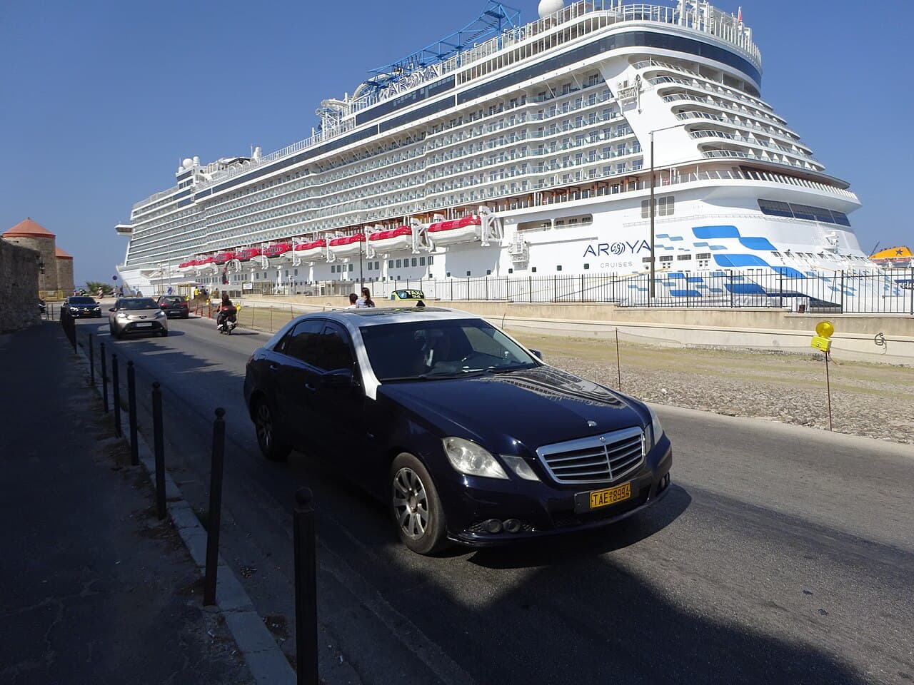 A taxi on the seafront road by the port of Rhodes Town, with a cruise ship behind