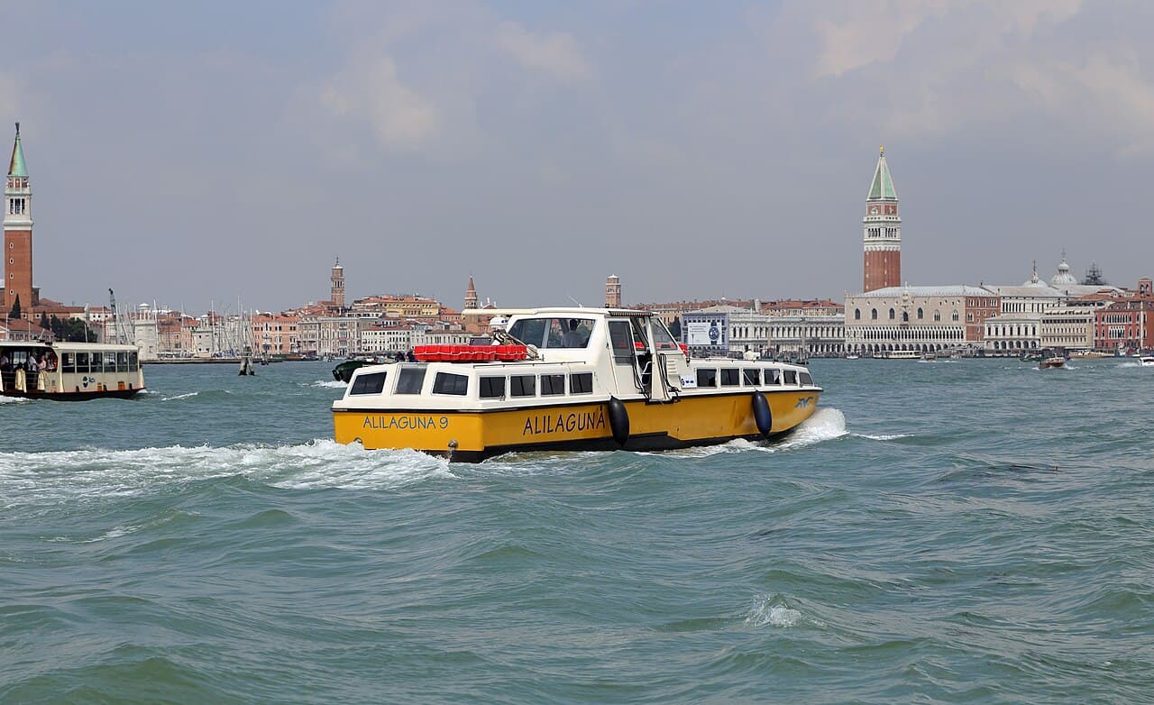 An Alilaguna water bus crossing the lagoon with the Venice skyline behind it