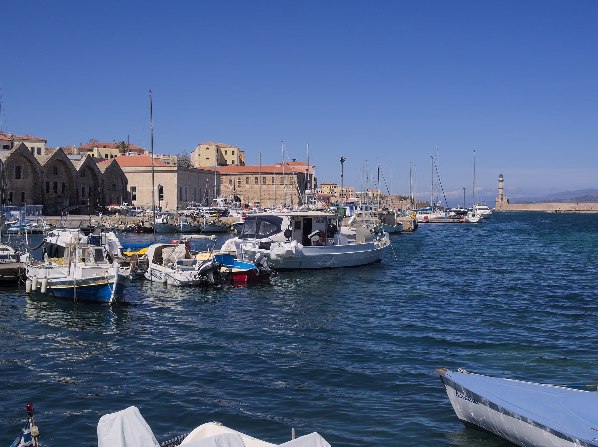 Boats in the old Venetian harbour of Chania, with the arched shipyards on the left and the lighthouse in the distance