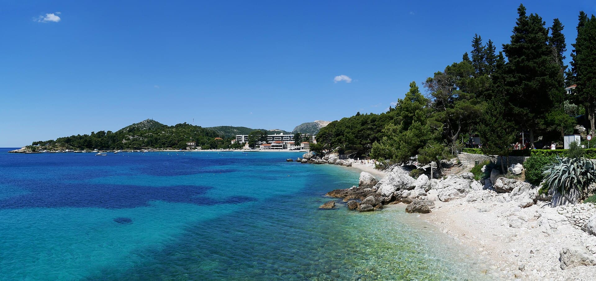 The clear turquoise water of the beach at Mlini, backed by pines