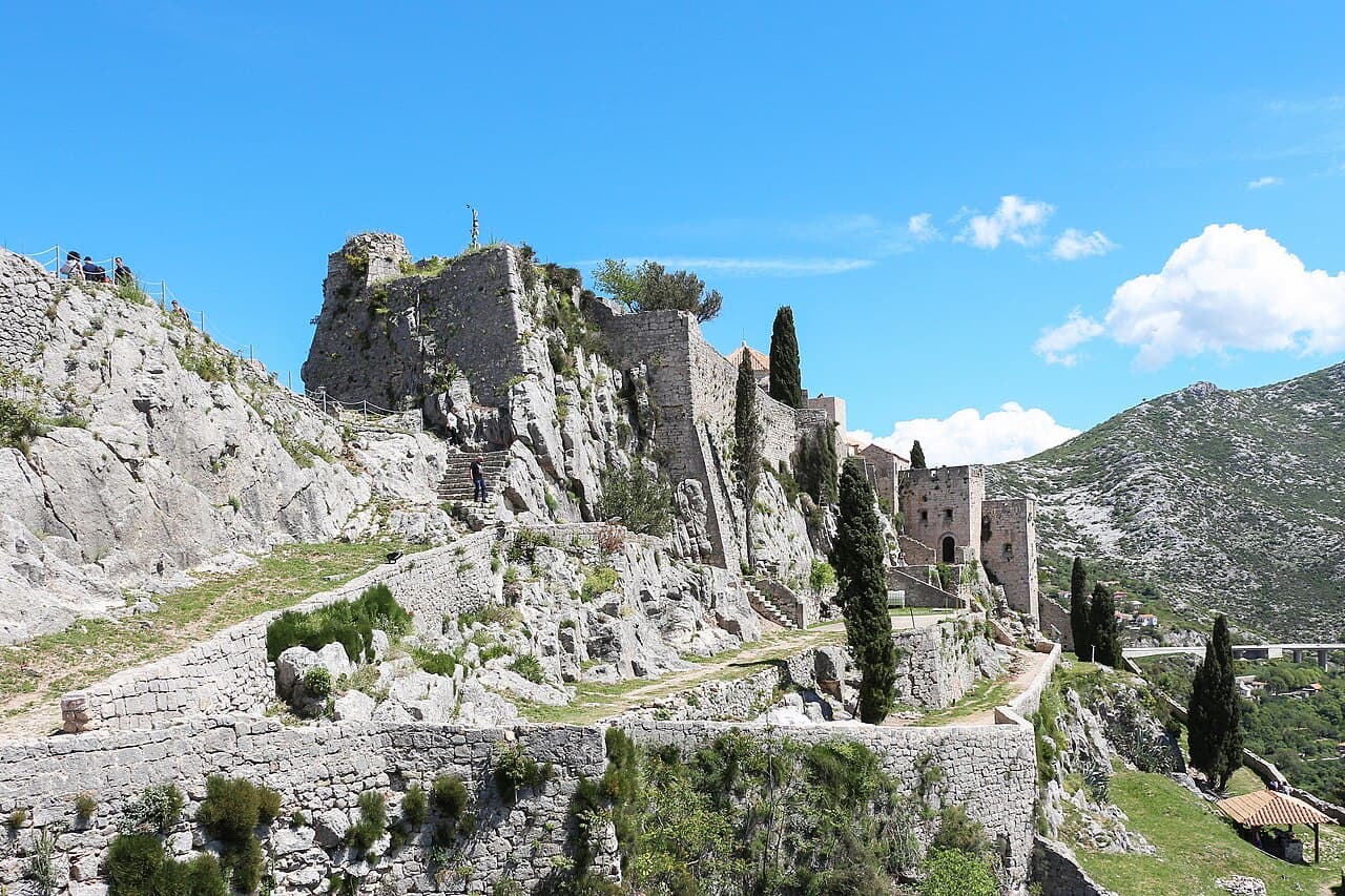 The walls of Klis Fortress running along a bare rock ridge above the pass